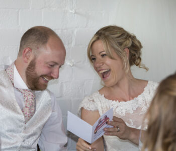 bride and groom laughing at a card given to them during speeches at their Bristol wedding