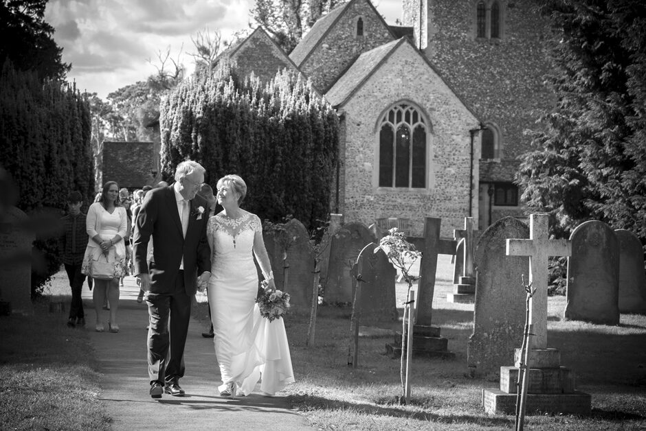 bride and groom walking together holding hands with guests following behind from Stoke Poges Church in Reading
