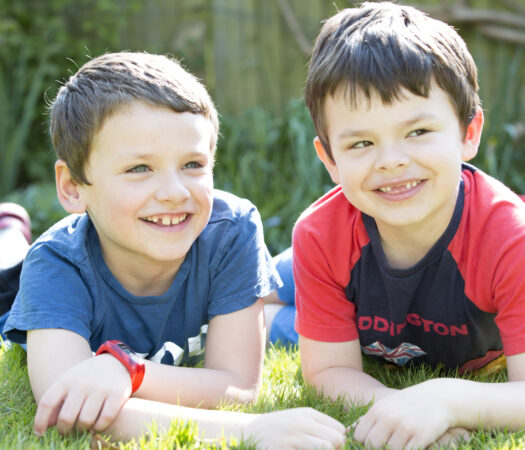 two boys sitting on their tummies smiling in their garden in Tonbridge, Kent. Captured by Kent family portrait photographer Victoria Green