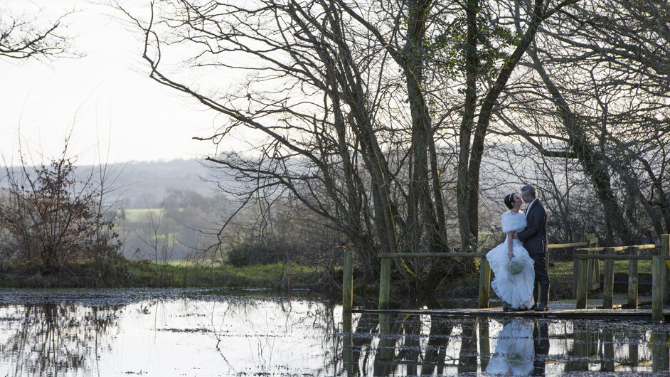 bride and groom sharing loving embrace by lake at Swallows Oast in Tunbridge Wells