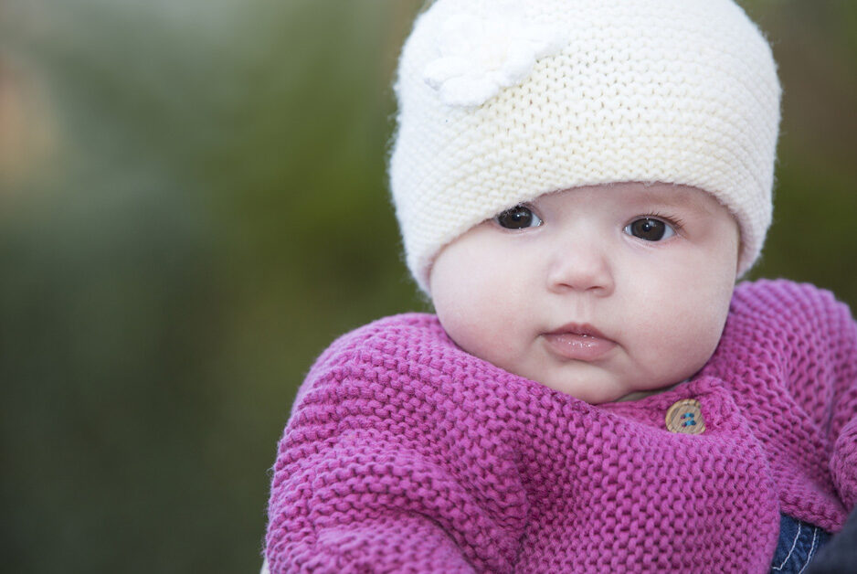 baby girl in wooly hat and pink cardigan in Plaxtol garden, Kent