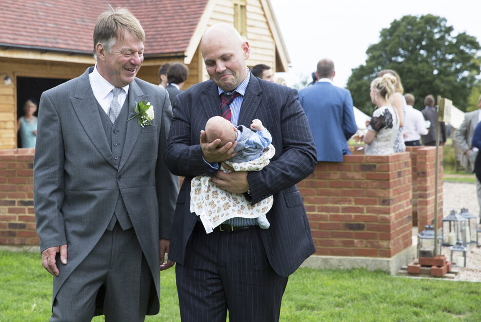 bride's father and friend admiring baby at Smarden village home wedding in Kent