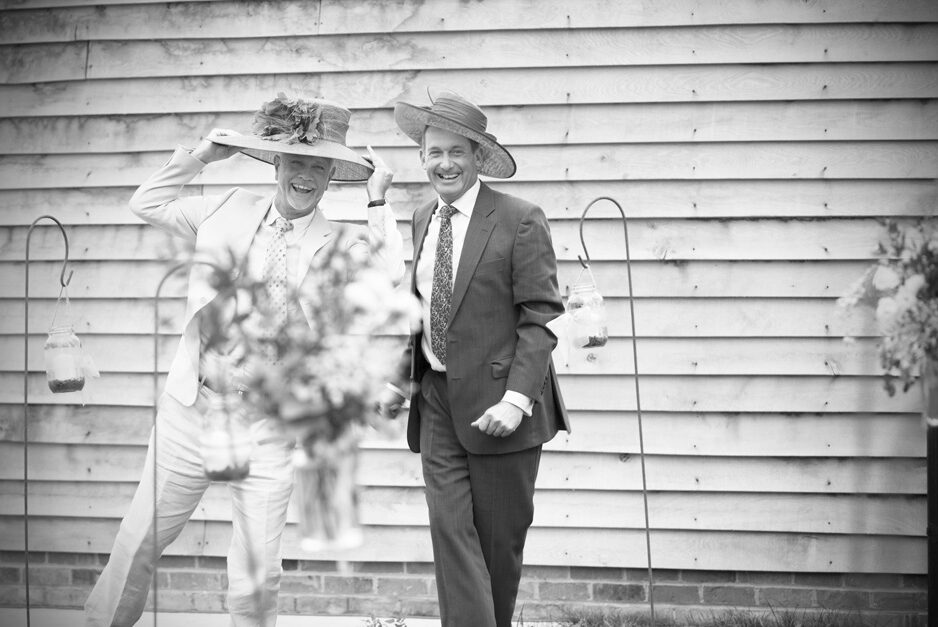two male guests larking about with ladies hats at Smarden village home wedding in Kent