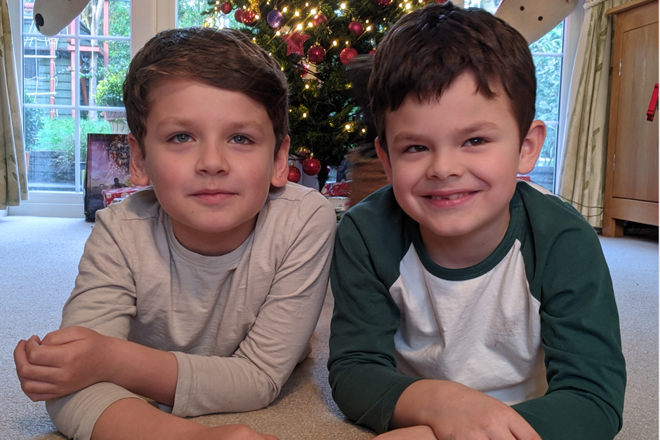 two little boys sitting on their tummies in front of the christmas tree