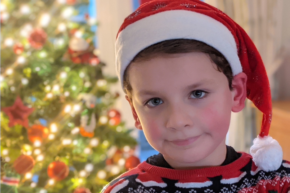 little boy with santa's hat standing by the christmas tree