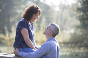 engagement shoot at Dunorlan Park - lady sitting on log with guy holding her, Tunbridge Wells in Kent