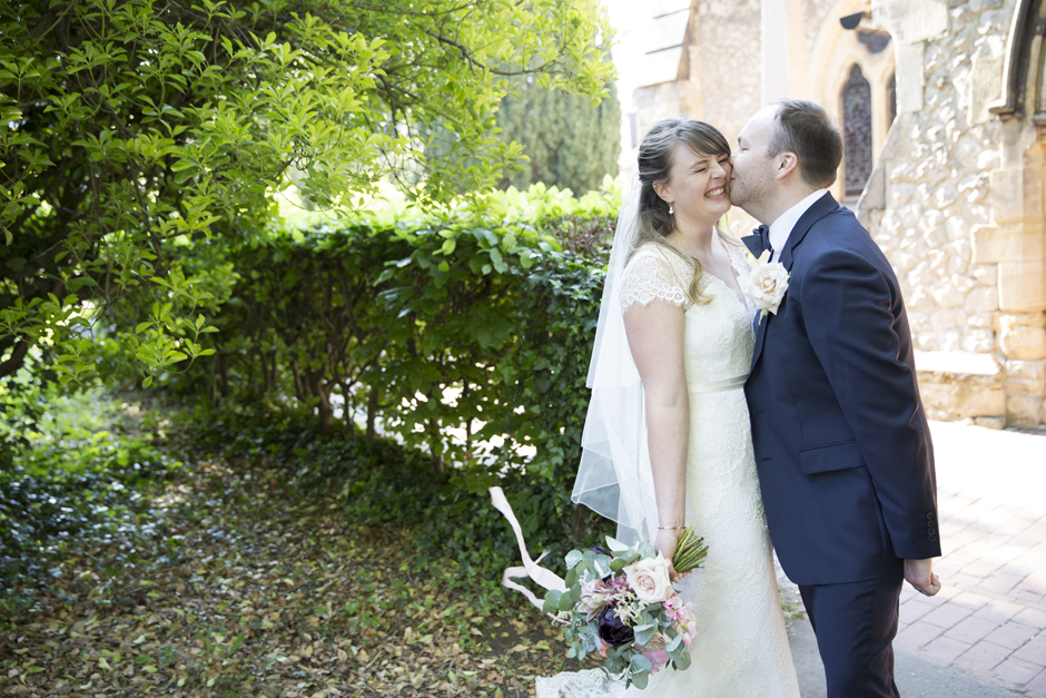Bride laughing being kissed by groom in wedding portrait outside of St Stephen's Church in Tonbridge, Kent