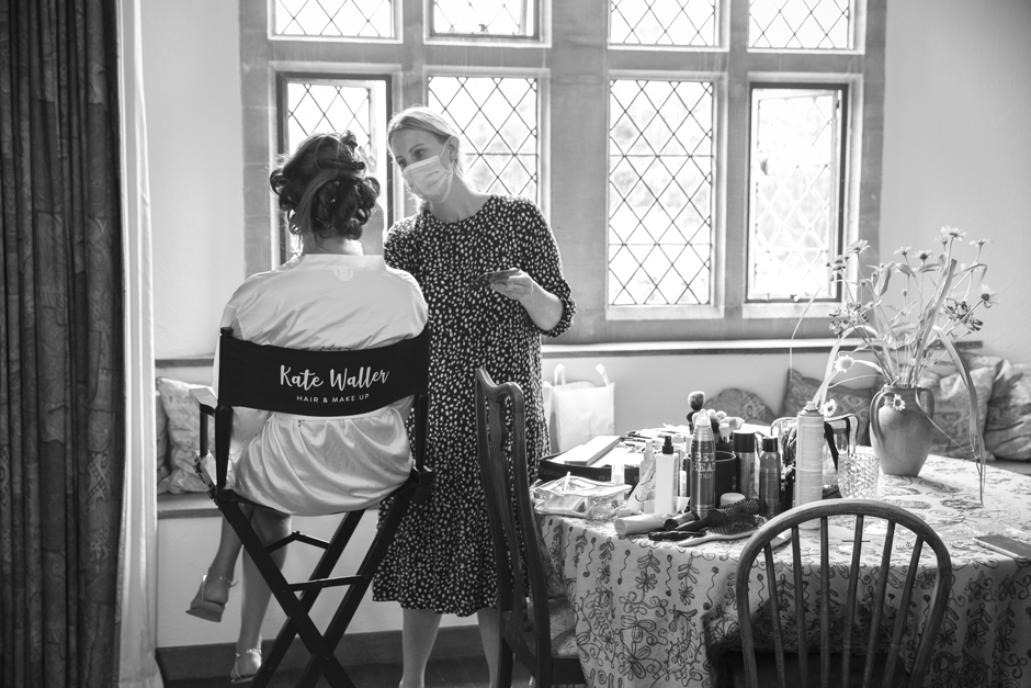 Back of bride sitting in make-up chair having her make-up done by Kate Waller wearing a face mask. Captured by Kent wedding photographer, Victoria Green.