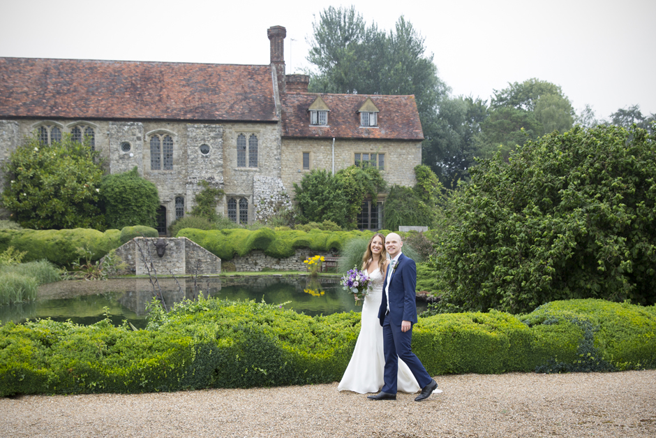 Bride and groom walking together at Nettlestead Place with house and lake in the background. Captured by Kent wedding photographer, Victoria Green.