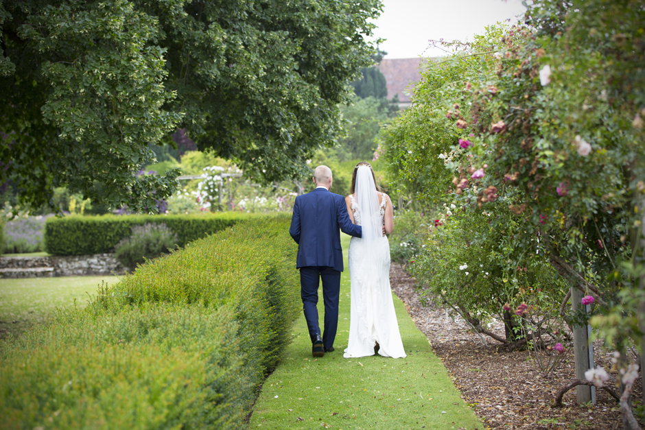 Back of wedding couple as they walk through the rose gardens at Nettlestead Place, Maidstone in Kent. Captured by wedding photographer, Victoria Green.