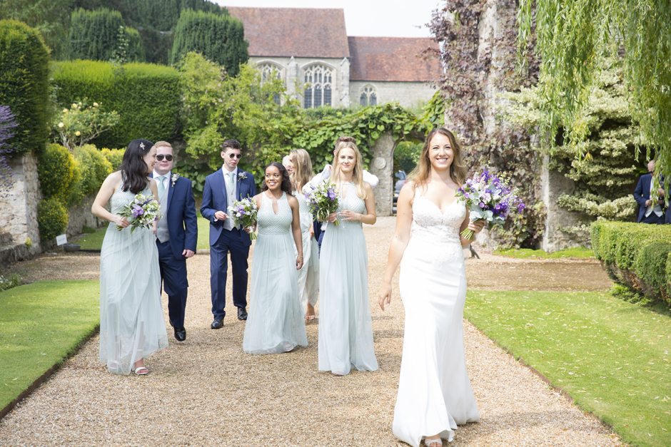 Bride and bridesmaids and groomsmen laughing walking in the grounds at Nettlestead Place. Captured by wedding photographer, Victoria Green.