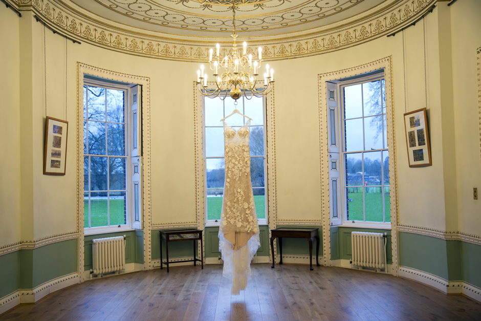 Wedding dress hanging from chandelier at Bradbourne House in East Malling, Kent. Captured by Victoria Green Photography.