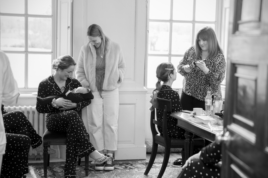 Bridesmaid having make-up done and bridesmaid holding baby during wedding morning bridal prep at Bradbourne House in East Malling, Kent.