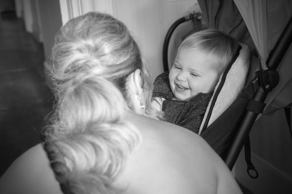 Baby sitting in pushchair laughing at bridesmaid at wedding morning at Bradbourne House, East Malling in Kent.