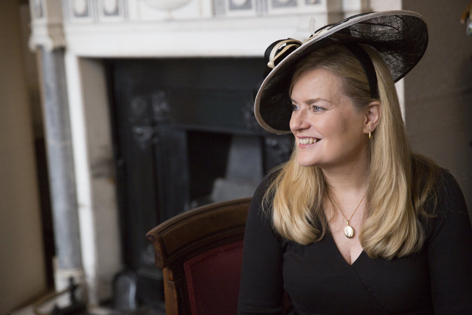 Bride's mother in black dress and hat looking on smiling during bridal prep at Bradbourne House in East Malling, Kent.