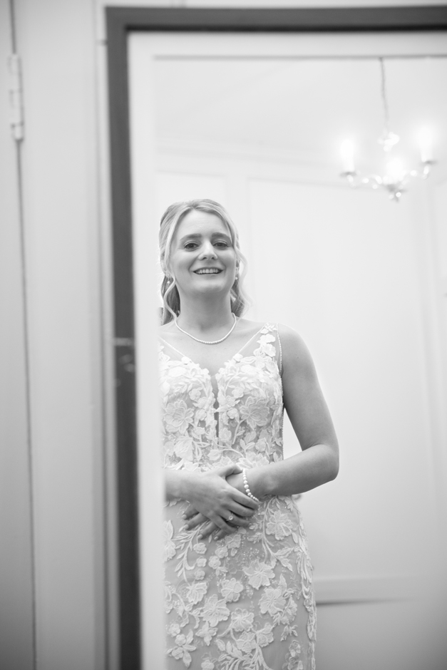 Bride looking in mirror smiling at her dress during wedding morning at Bradbourne House in East Malling, Kent.