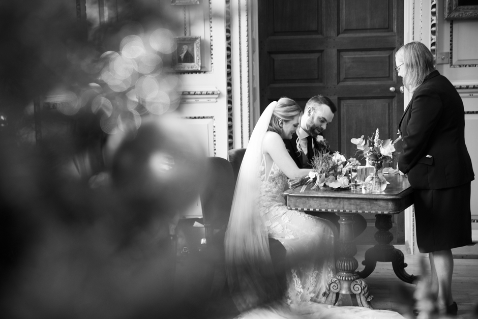 Side shot of bride and groom signing the register during wedding ceremony at Bradbourne House in East Malling, Kent.