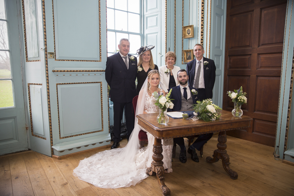 Bride & Groom sitting at table after signing the register with all witnesses standing behind them at wedding ceremony at Bradbourne House in East Malling, Kent.
