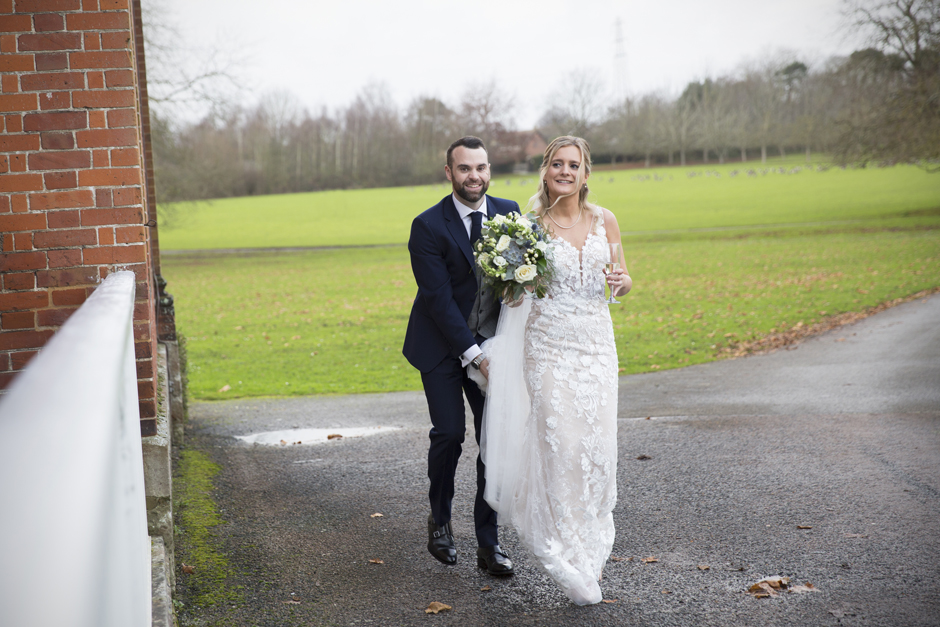 Groom holding bride's dress as they walking around the grounds at Bradbourne House in East Malling, Kent. Captured by Kent wedding photographer Victoria Green.