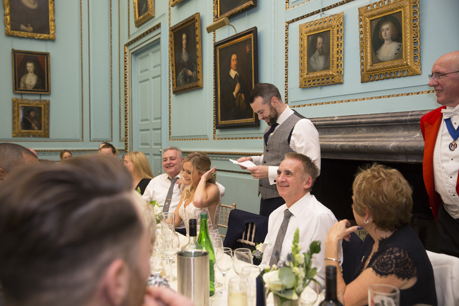 Groom standing and laughing reading speech during wedding breakfast speeches at Bradbourne House in East Malling, Kent.
