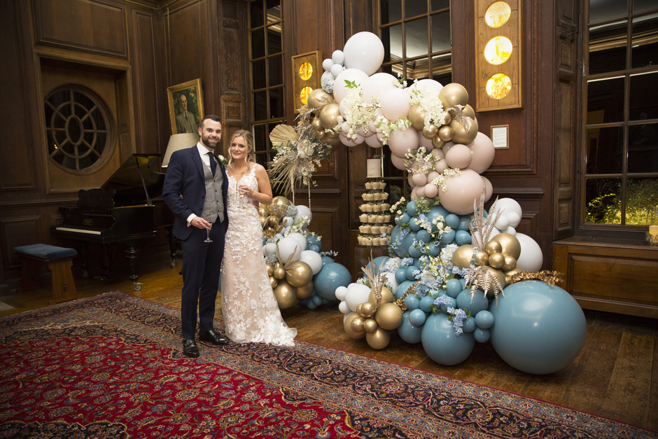 Bride and Groom standing by balloon arch and cake under arch at Bradbourne House library at East Malling in Kent.