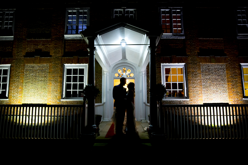 Bride and Groom standing under canopy at nighttime as silhouettes lit only by outside ambient lighting. Captured at Bradbourne House, East Malling in Kent by Victoria Green Photography.