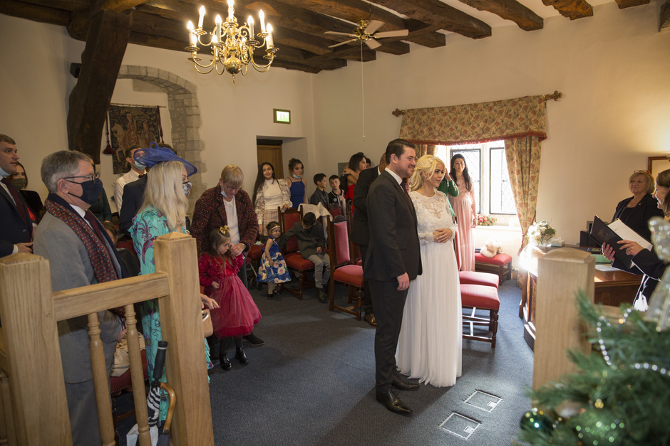 Bride and Groom standing with guests in the background in The Undercroft register office room at Archbishop's Palace in Maidstone, Kent.