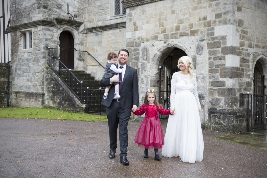 Bride and Groom walking holding hands with their children outside Archbishop's Palace, Maidstone in Kent. Captured by Victoria Green Photography.