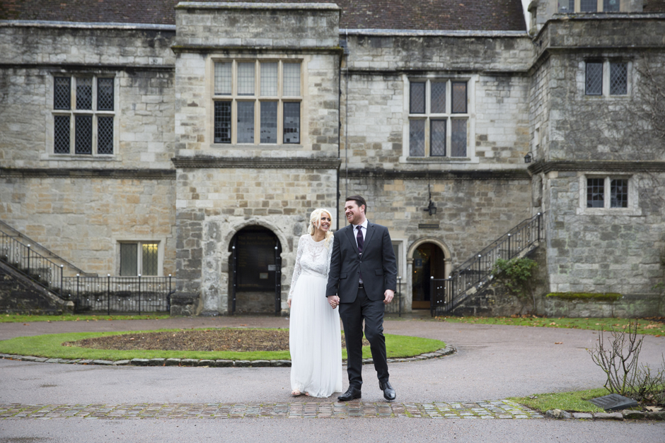 Bride and Groom holding hands laughing standing in front of Archbishop's Palace Register Office in Maidstone, Kent. Captured by Victoria Green wedding photographer.