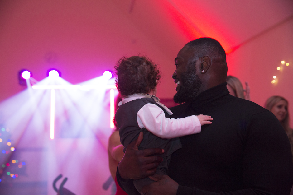 Male wedding guest holding baby looking at disco lights at evening wedding reception in Sevenoaks, Kent.