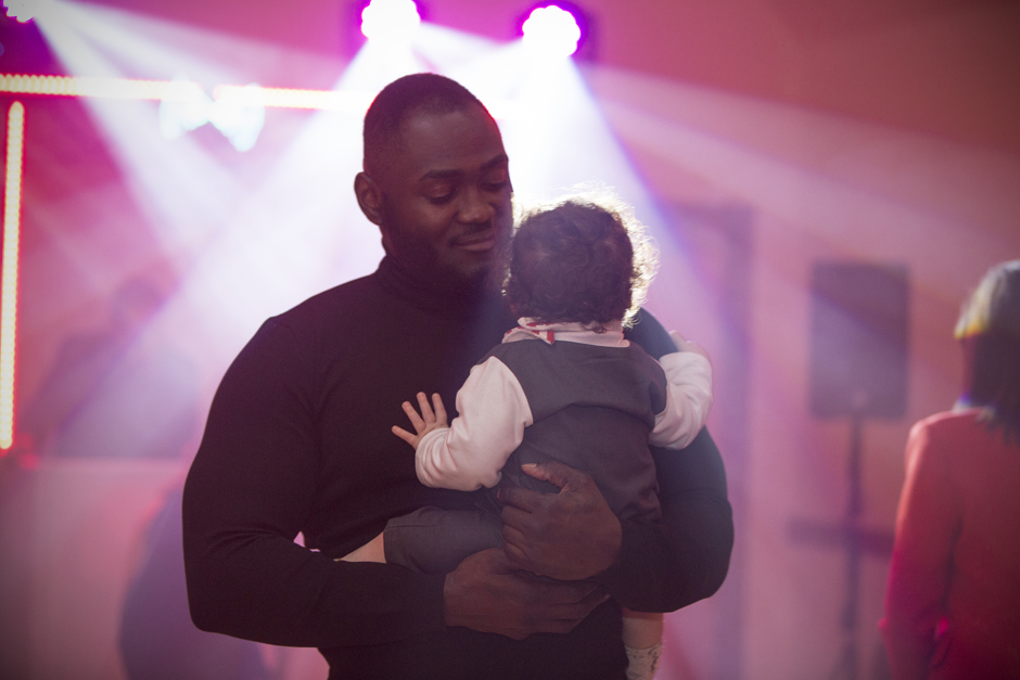 Male wedding guest holding baby amongst disco lights at evening wedding reception in Sevenoaks, Kent.