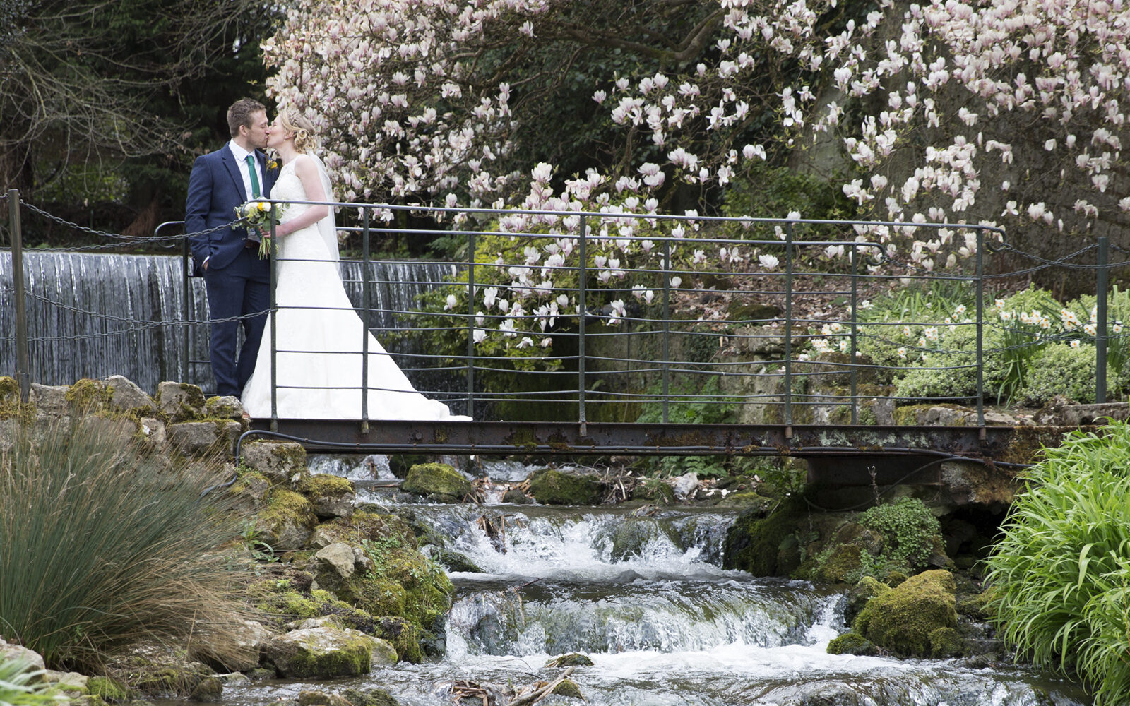 Bride and Groom on bridge overlooking waterfall at The Orangery in Maidstone, Kent. Captured by Kent wedding photographer Victoria Green.