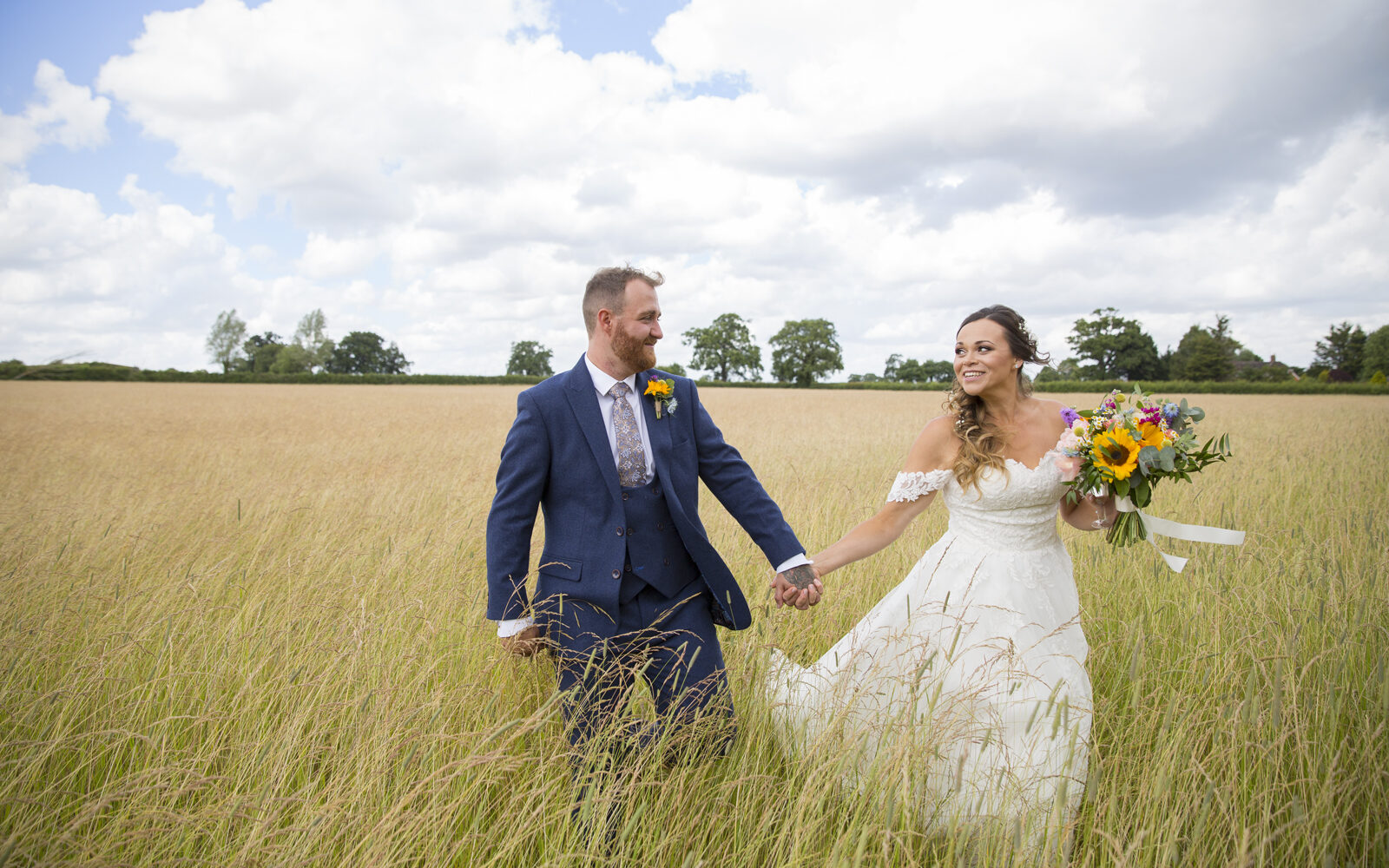 Bride & Groom holding hands walking through a field looking at each other, captured by Kent wedding photographer Victoria Green.